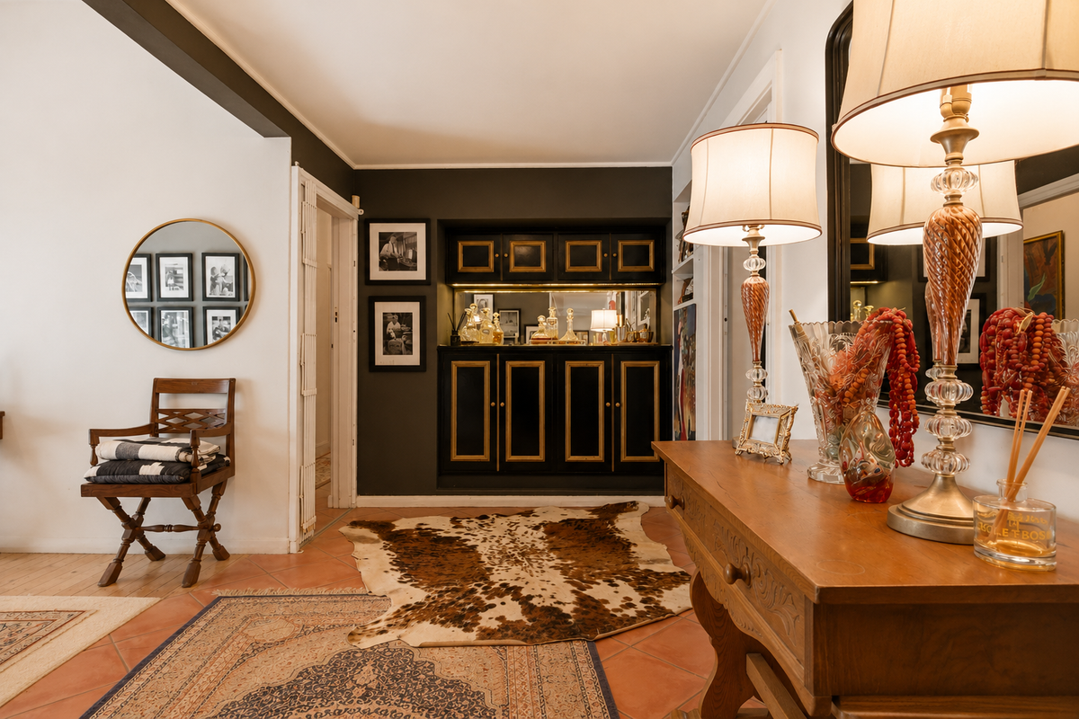 A living area featuring a built-in bar cabinet with gold detailing, set against a dark accent wall with terracotta tiled flooring.