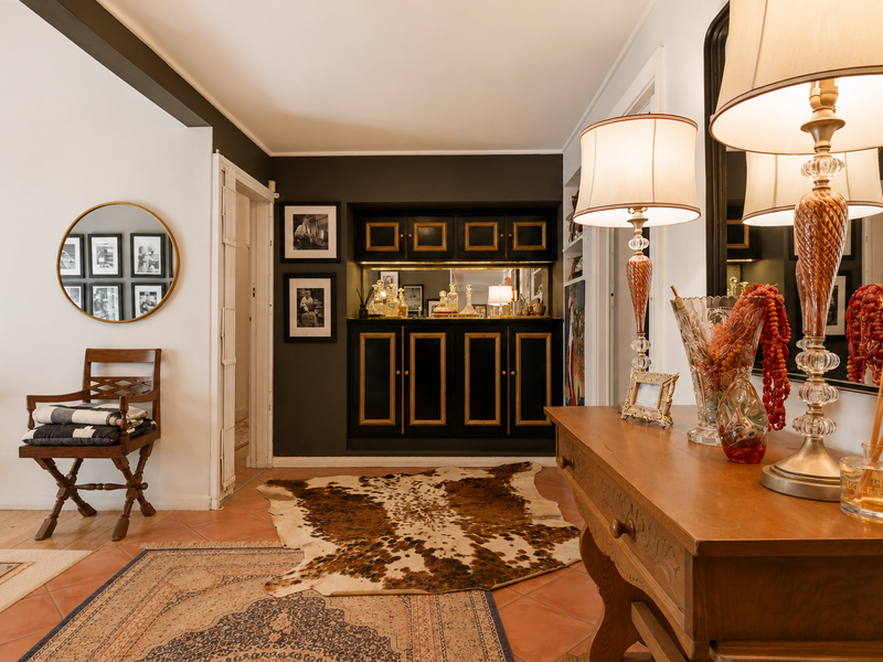 A living area featuring a built-in bar cabinet with gold detailing, set against a dark accent wall with terracotta tiled flooring.