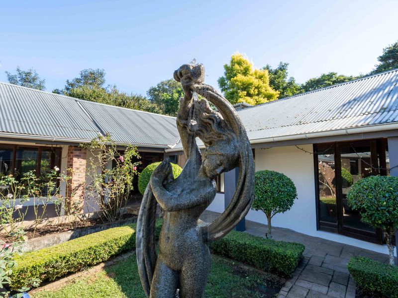 A well-maintained rear courtyard featuring a central stone fountain, paved pathways, and landscaped garden beds set against the property's exterior facade.