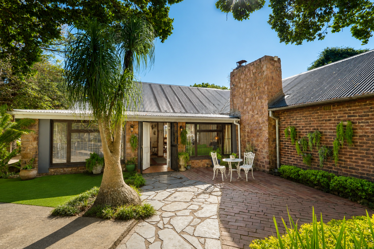 A charming rear exterior view featuring a stone chimney, corrugated metal roof, and a combination of stone and brick paved patio areas.