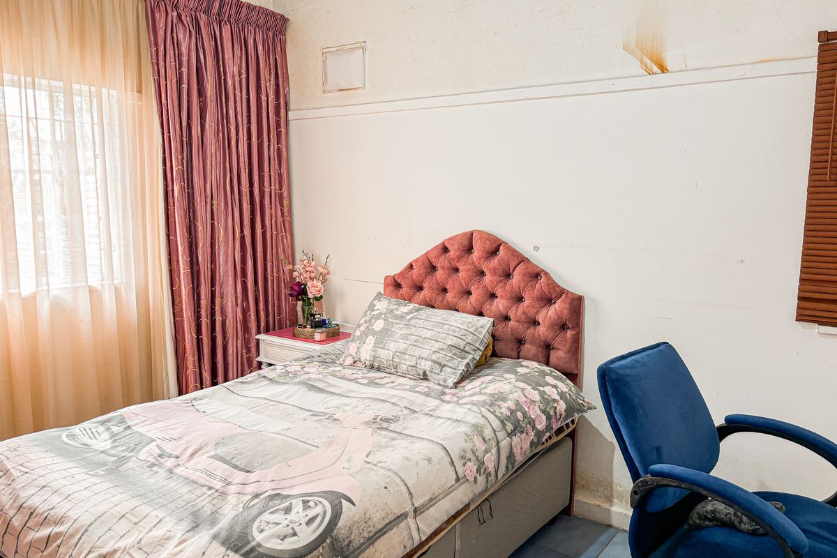 A bedroom featuring tiled flooring and visible wall damage, including water staining and peeling paint, requiring maintenance and cosmetic updates.