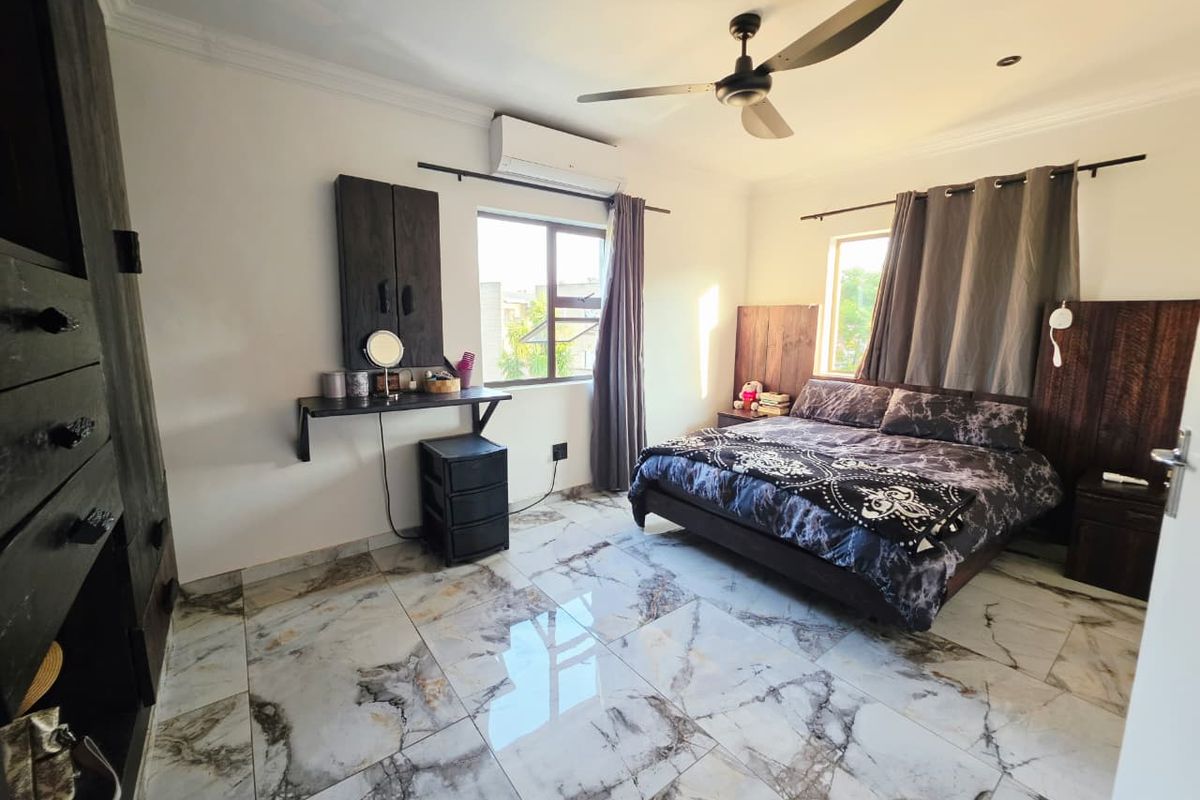 Spacious bedroom featuring polished marble-look floor tiles, a ceiling fan, and a wall-mounted air conditioning unit.