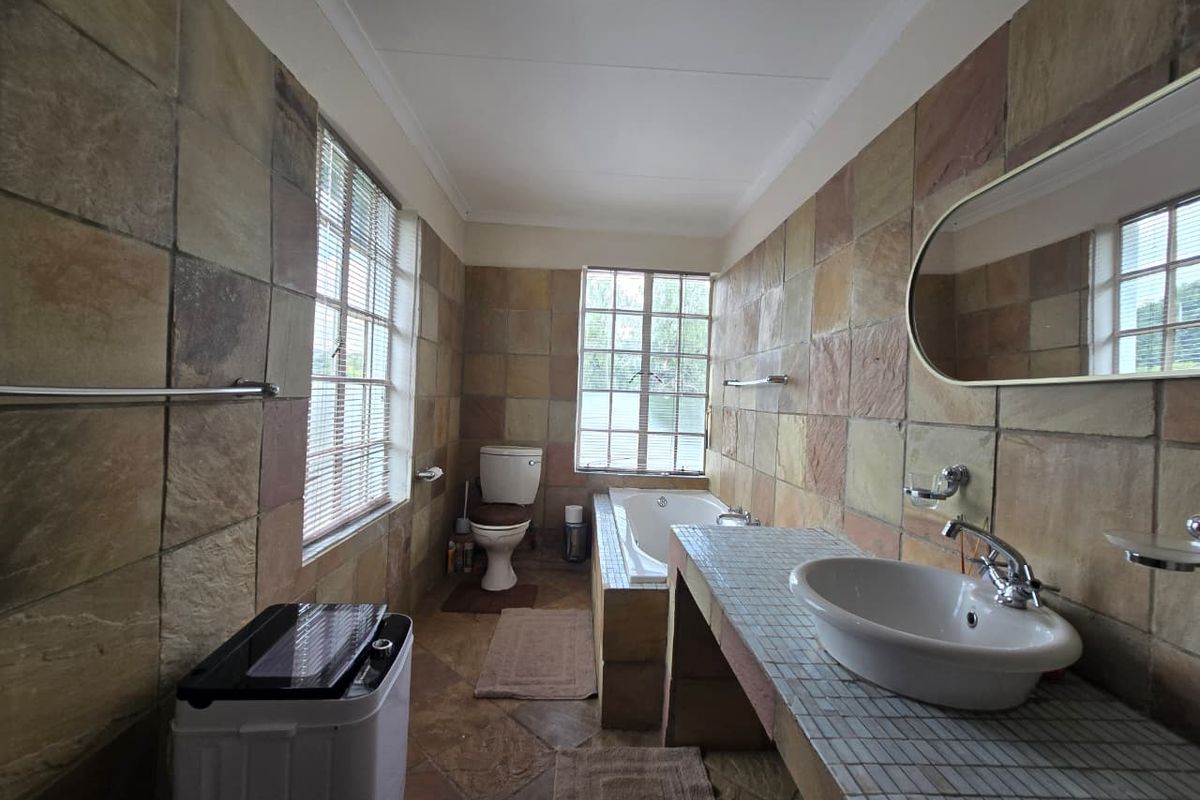 A functional bathroom featuring a built-in bathtub, tiled vanity with a ceramic basin, and full-height stone-style wall tiling.