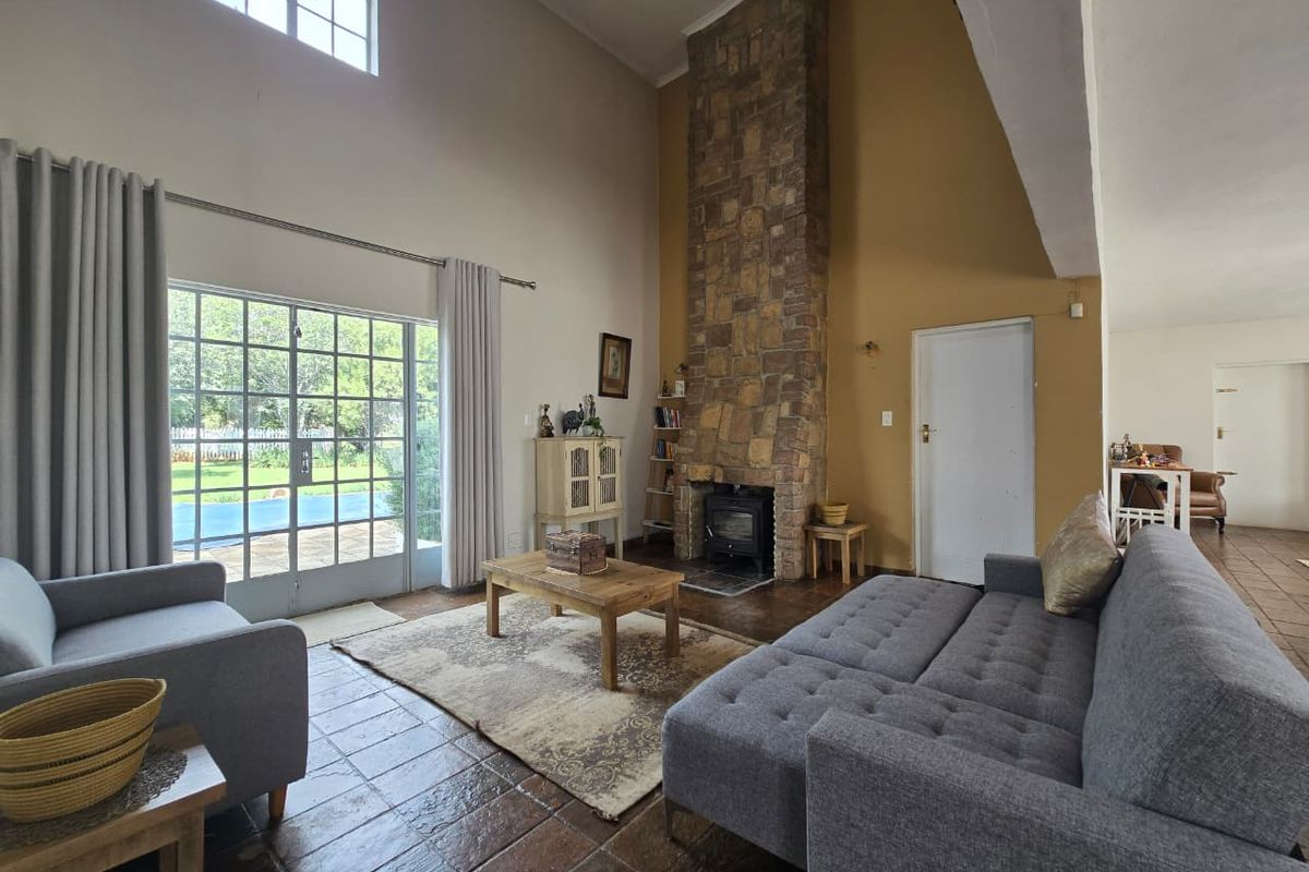 Spacious living room featuring a double volume ceiling, a prominent stone fireplace with a wood-burning stove, and direct access to the garden through french doors.