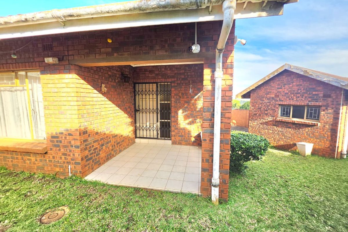 A rear view of a face brick house featuring a covered tiled patio area and a separate brick outbuilding set in a grassy yard.