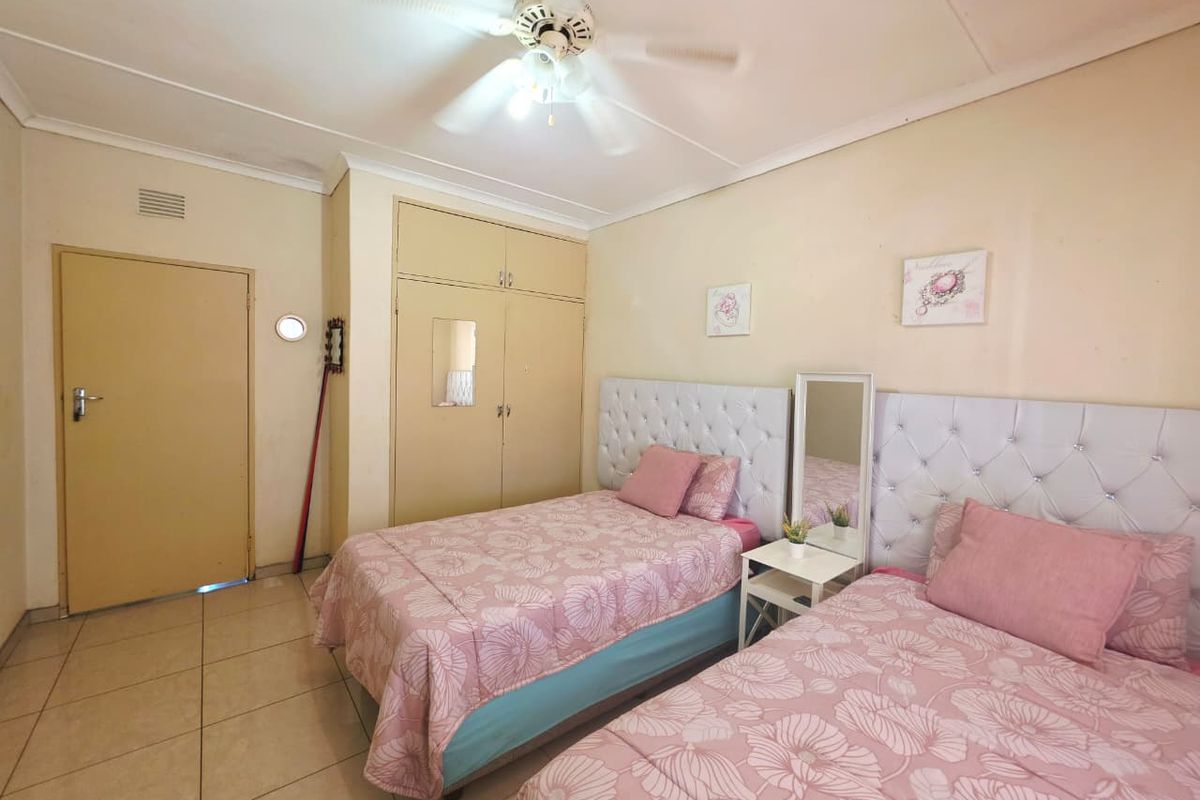 A bedroom featuring tiled flooring, built-in cupboards, and a ceiling fan, offering a functional space with potential for cosmetic updates.