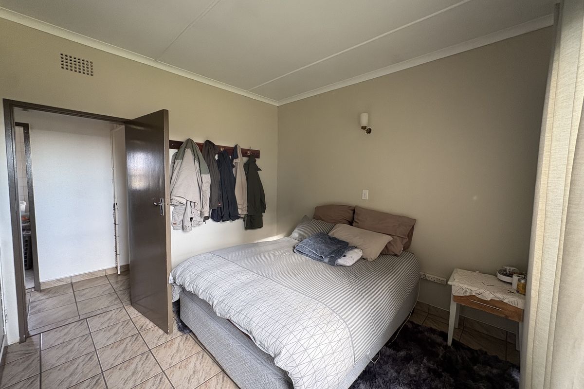 A functional bedroom featuring tiled flooring, neutral wall tones, and a wall-mounted light fixture, providing a simple and practical living space.