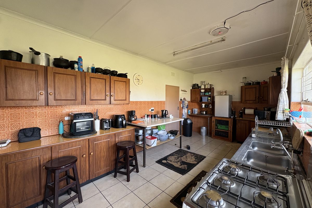 A spacious kitchen featuring wooden cabinetry, a gas hob, double stainless steel sink, and tiled finishes, offering significant potential for a modern renovation.