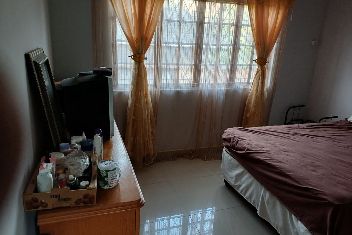 A standard bedroom featuring tiled flooring and window security bars, providing a functional space with natural light.