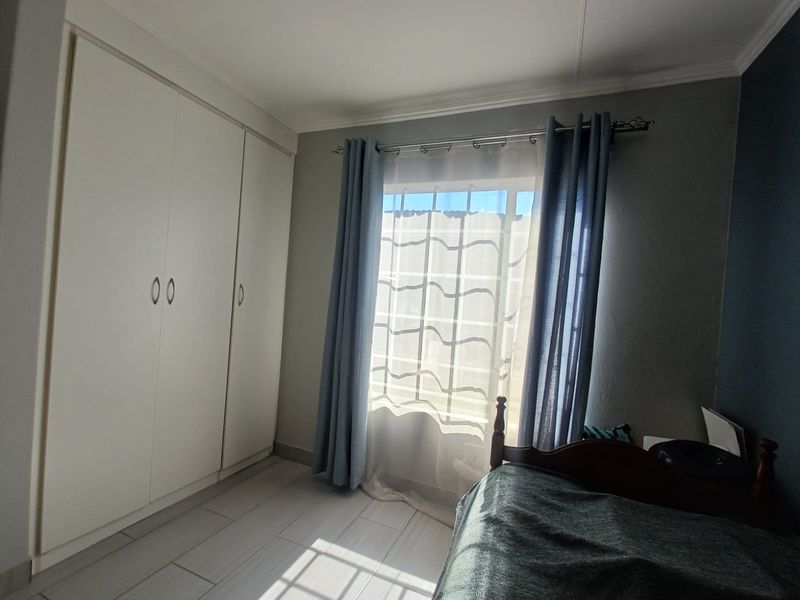 A well-maintained bedroom featuring built-in cupboards, tiled flooring, and a window with security bars, offering a clean and functional living space.