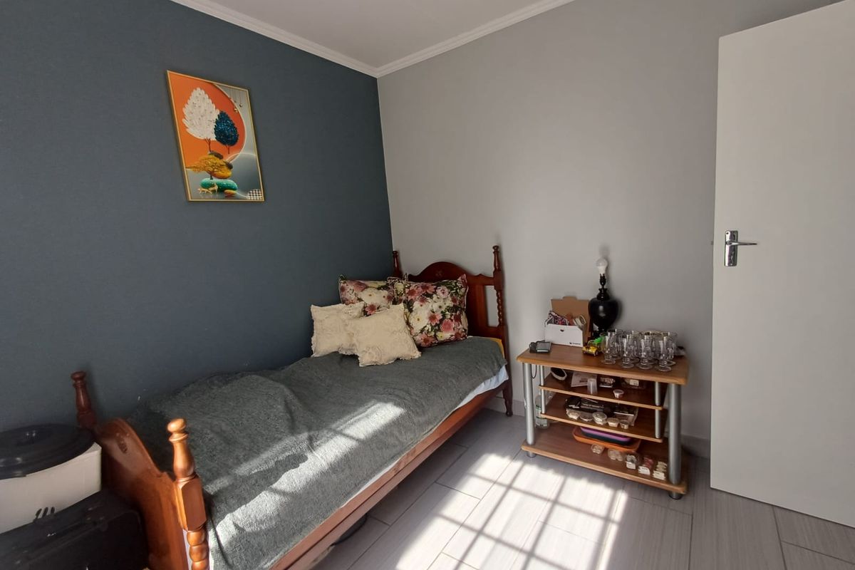 A well-lit bedroom featuring neutral wall tones, a dark blue accent wall, tiled flooring, and classic cove cornicing.