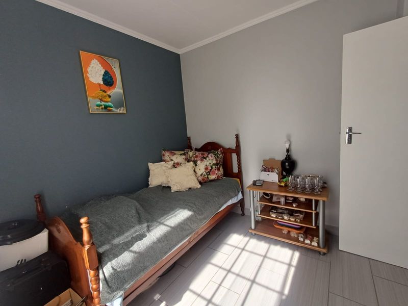 A well-lit bedroom featuring neutral wall tones, a dark blue accent wall, tiled flooring, and classic cove cornicing.