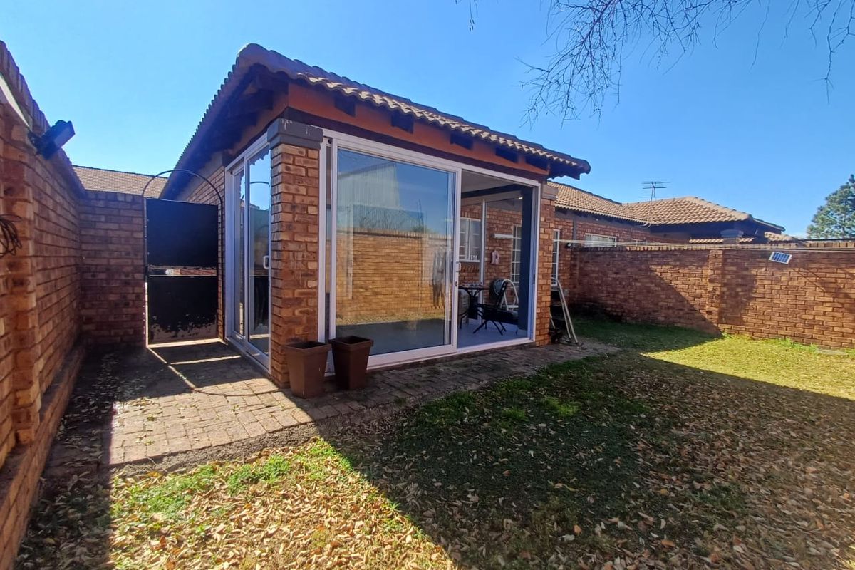 Rear view of the townhouse featuring a brick-walled garden, paved patio area, and a covered structure with sliding glass doors.