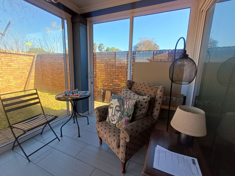 A bright, enclosed patio area featuring large sliding glass doors, tiled flooring, and views of the private brick-walled garden.
