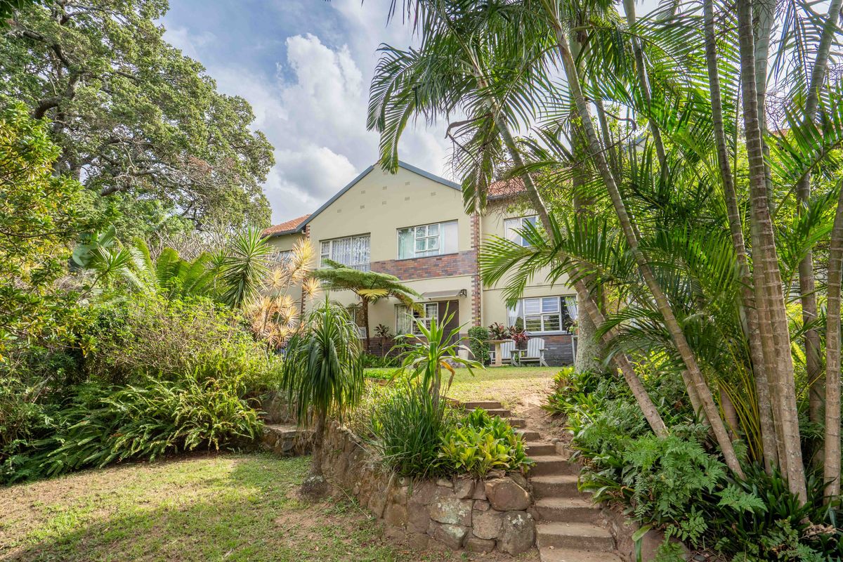 A rear view of the property featuring a landscaped garden, stone retaining wall, and stone steps leading up to the building facade.