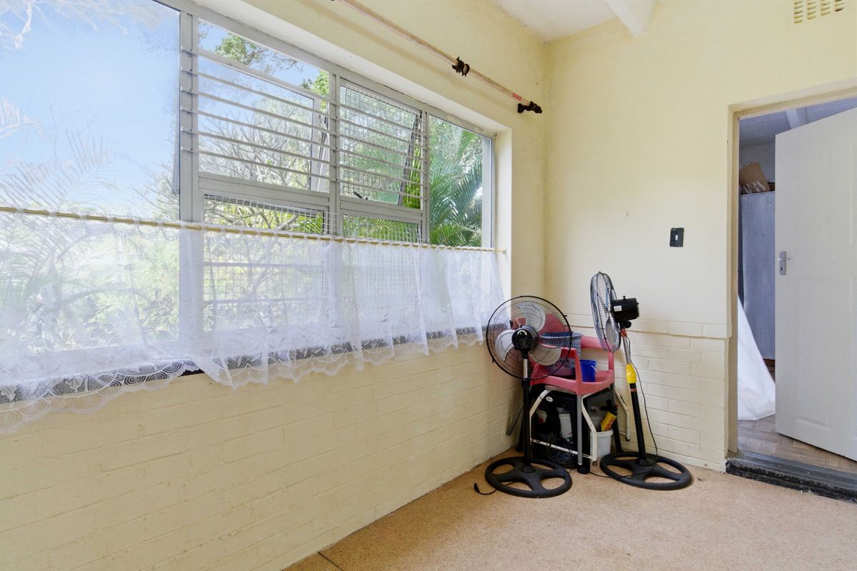 A sunlit living area featuring large louvre windows, painted brick walls, and carpeted flooring, offering a blank canvas for renovation.