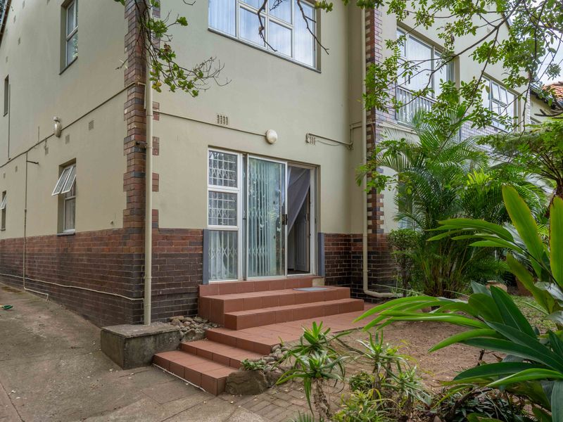 Rear view of the flat featuring a brick facade, tiled entrance steps, and a sliding glass door with security gate access.