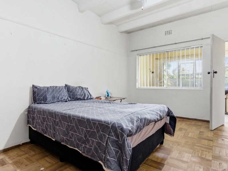 A bedroom featuring parquet flooring, exposed ceiling beams, and a window with security bars, offering a functional space with potential for cosmetic updates.