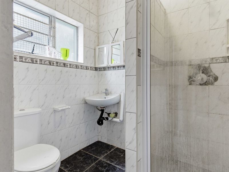 A compact bathroom featuring a wall-mounted basin, toilet, and a shower enclosure with tiled finishes throughout.