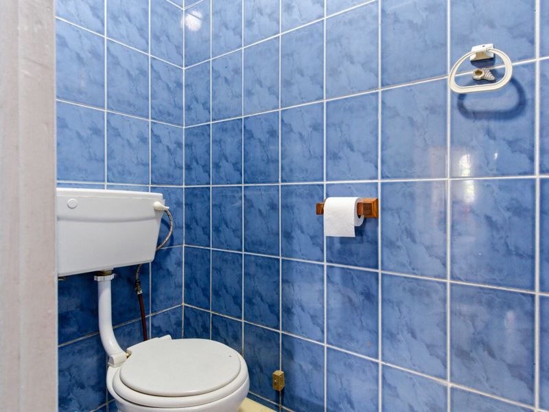 A compact bathroom featuring blue wall tiles and a standard toilet suite, requiring cosmetic updates to modernize the space.