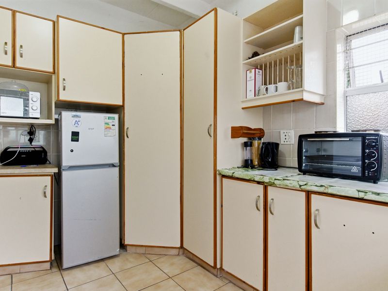 A functional kitchen featuring dated laminate cabinetry, tiled flooring, and a tiled backsplash, offering potential for a modern renovation.