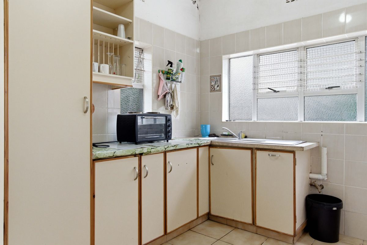 A functional kitchen featuring dated cabinetry, laminate countertops, a stainless steel sink, and tiled splashbacks with louvered windows for natural ventilation.