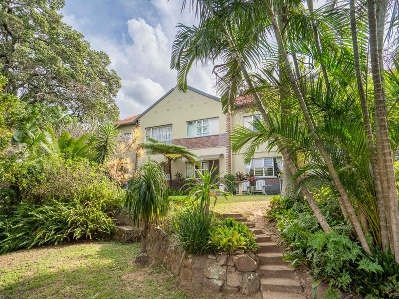 A rear view of the property featuring a landscaped garden, stone retaining wall, and stone steps leading up to the building facade.