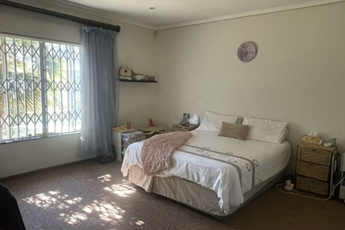 A spacious bedroom featuring recessed lighting, a large window with security bars, and built-in shelving, offering a comfortable and functional living space.