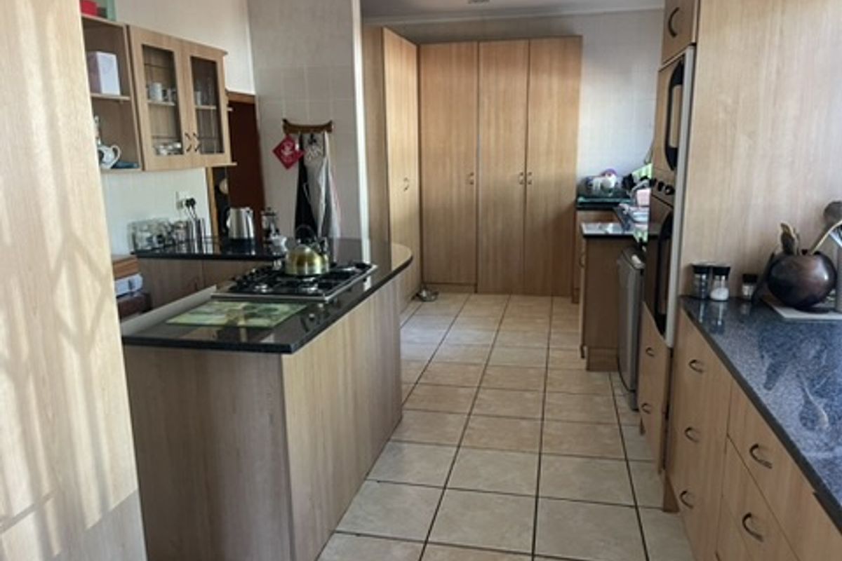 A functional kitchen featuring light wood cabinetry, granite countertops, a gas hob, built-in oven, and ample storage space with tiled flooring.