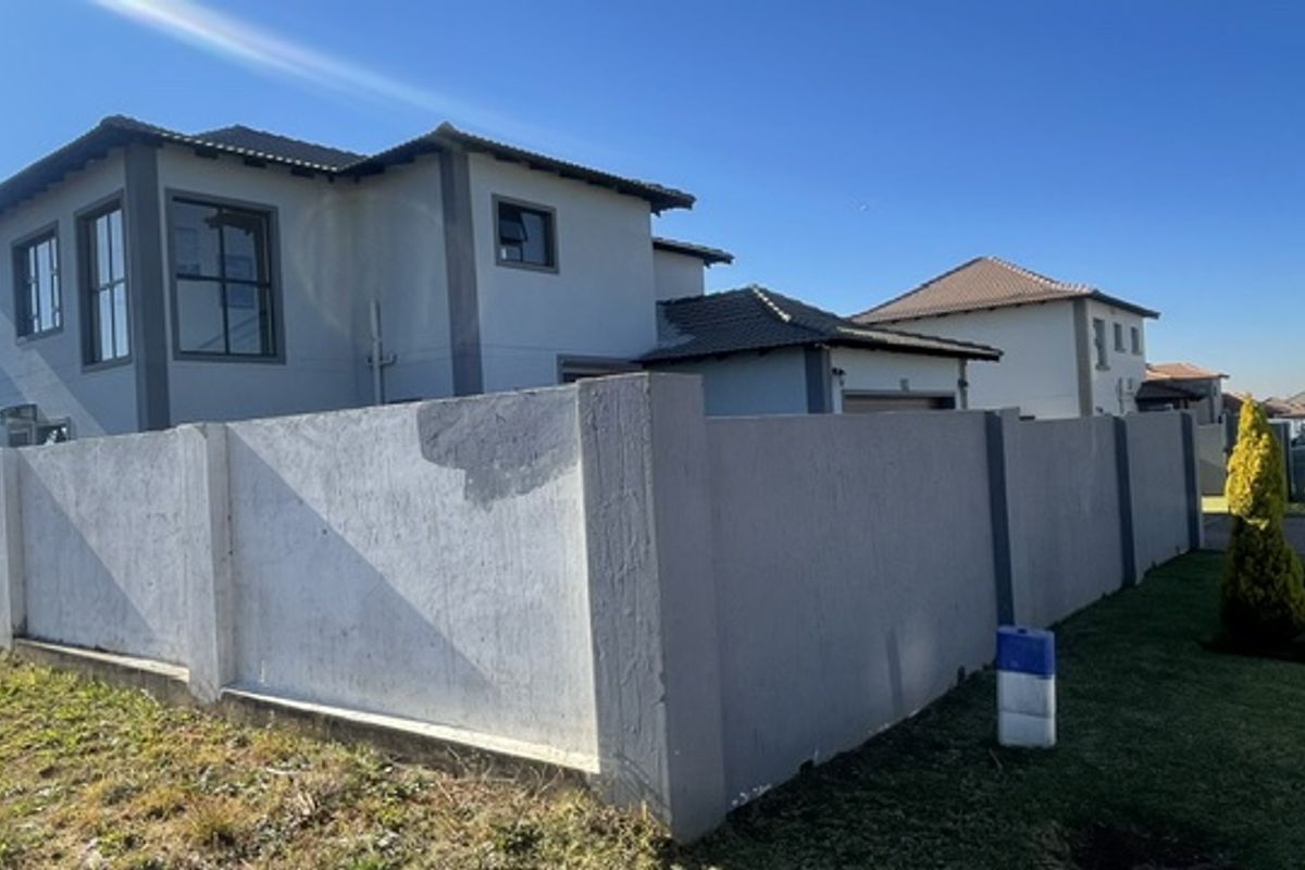 Rear view of a double-storey cluster home featuring a tiled roof, aluminium window frames, and a perimeter boundary wall.