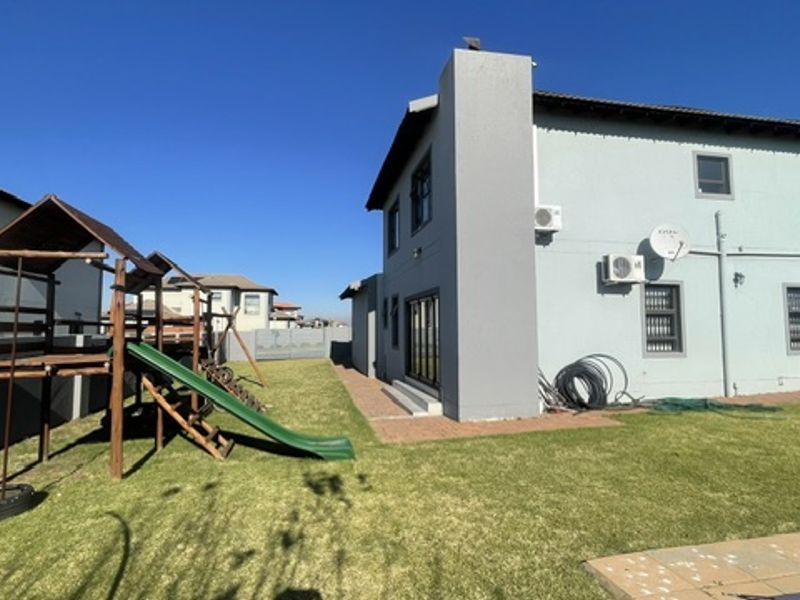Rear view of the cluster property featuring a paved patio area, well-maintained lawn, and exterior wall-mounted air conditioning units.