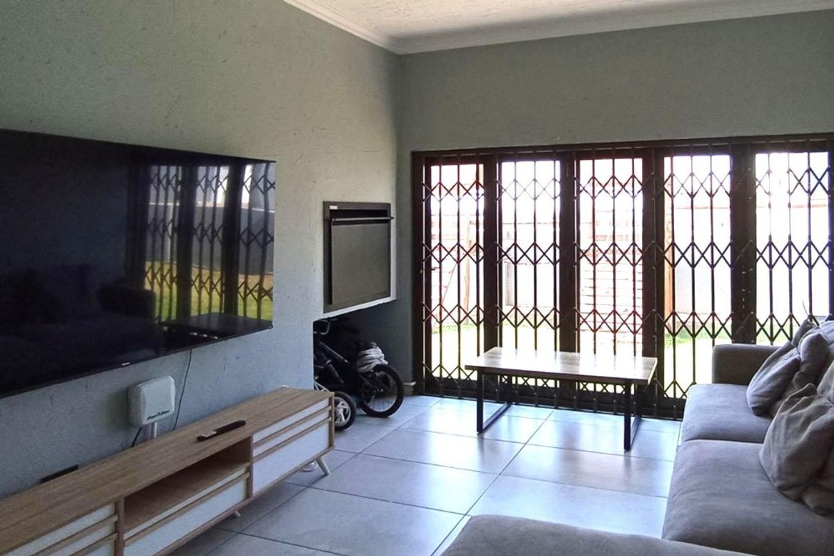 A living room featuring tiled flooring, a built-in fireplace, and large sliding doors with security gates leading to the exterior.