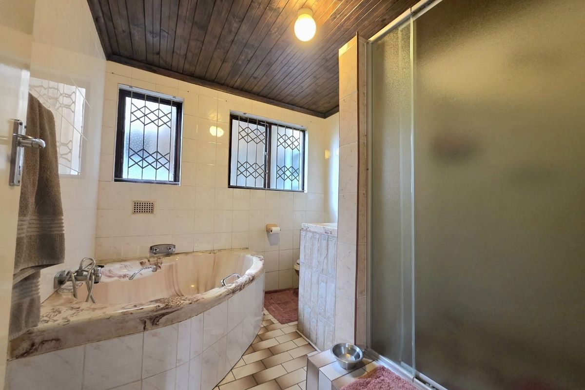 A dated bathroom featuring a built-in corner bathtub, separate shower enclosure, tiled surfaces, and a timber-paneled ceiling.
