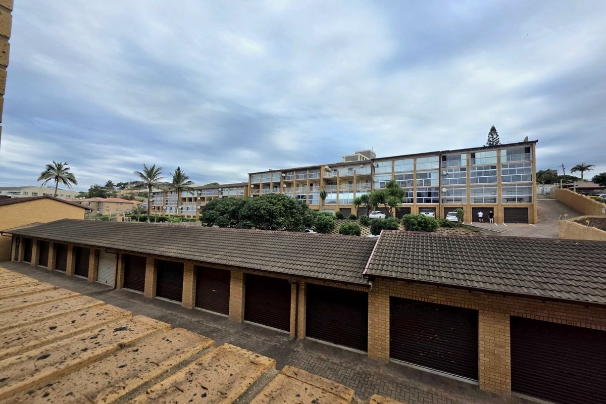 Exterior view of an apartment complex featuring a row of garages with tiled roofs and multi-story residential units with balconies.