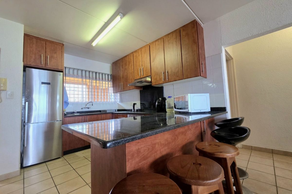 A functional kitchen featuring wooden cabinetry, granite countertops, a breakfast bar, and tiled flooring, providing a practical space for cooking and casual dining.