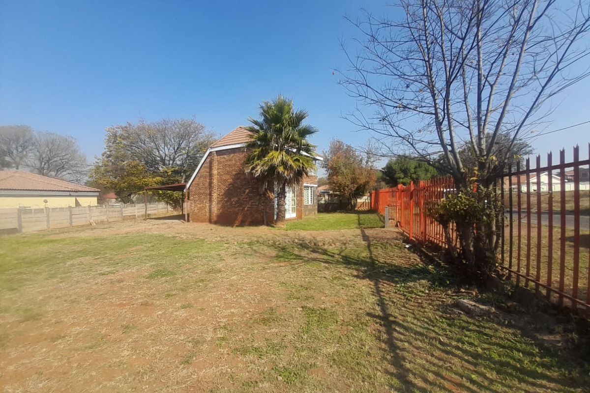A view of the rear garden area featuring a brick house, established lawn, and secure metal palisade perimeter fencing.