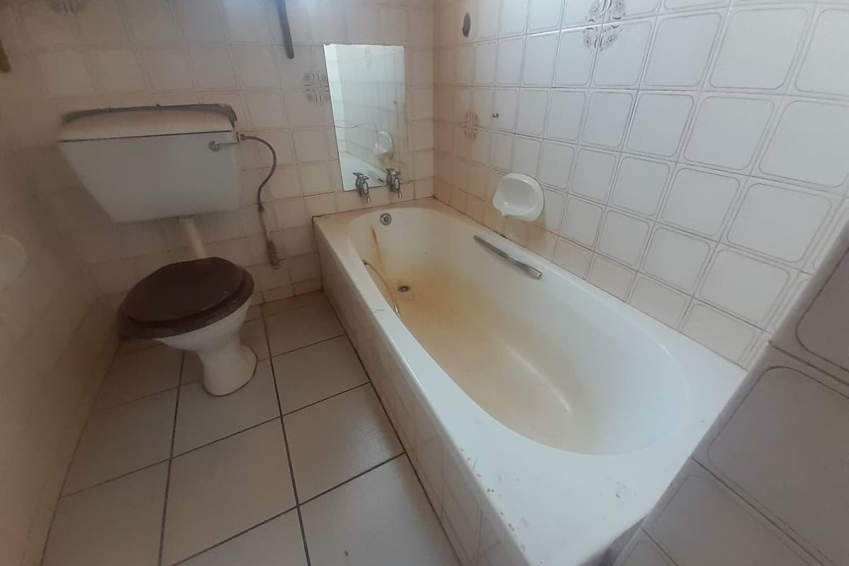 A dated bathroom featuring a standard bathtub, toilet, and full-height ceramic wall tiling, requiring significant refurbishment and deep cleaning of fixed fixtures.