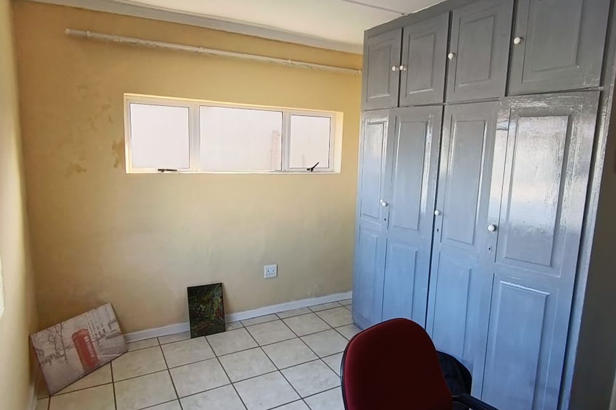 A bedroom featuring tiled flooring, built-in cupboards, and a horizontal window. The room requires cosmetic updates to the wall finishes.