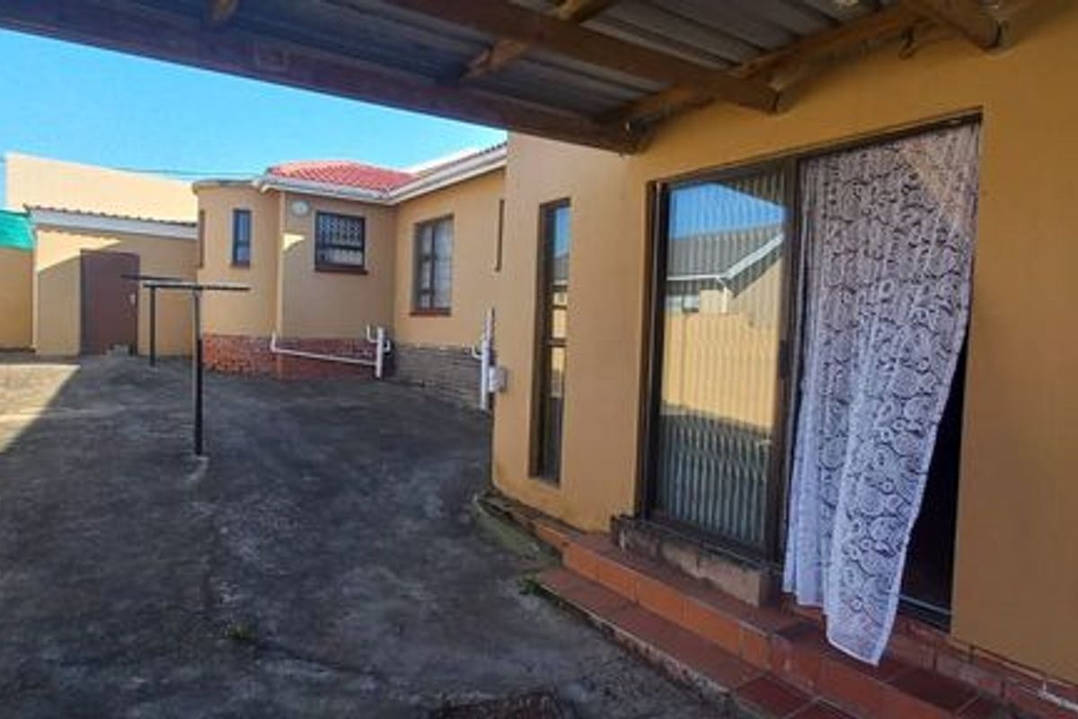 Rear exterior view showing a covered patio area, concrete paved yard, boundary walls, and access to the home via a sliding glass door.