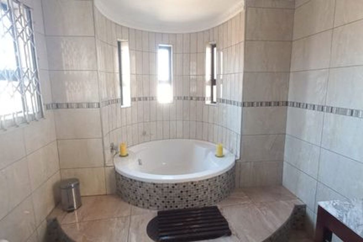 A spacious bathroom featuring a built-in corner bathtub, tiled finishes, and a vanity basin, offering a clean and functional layout.