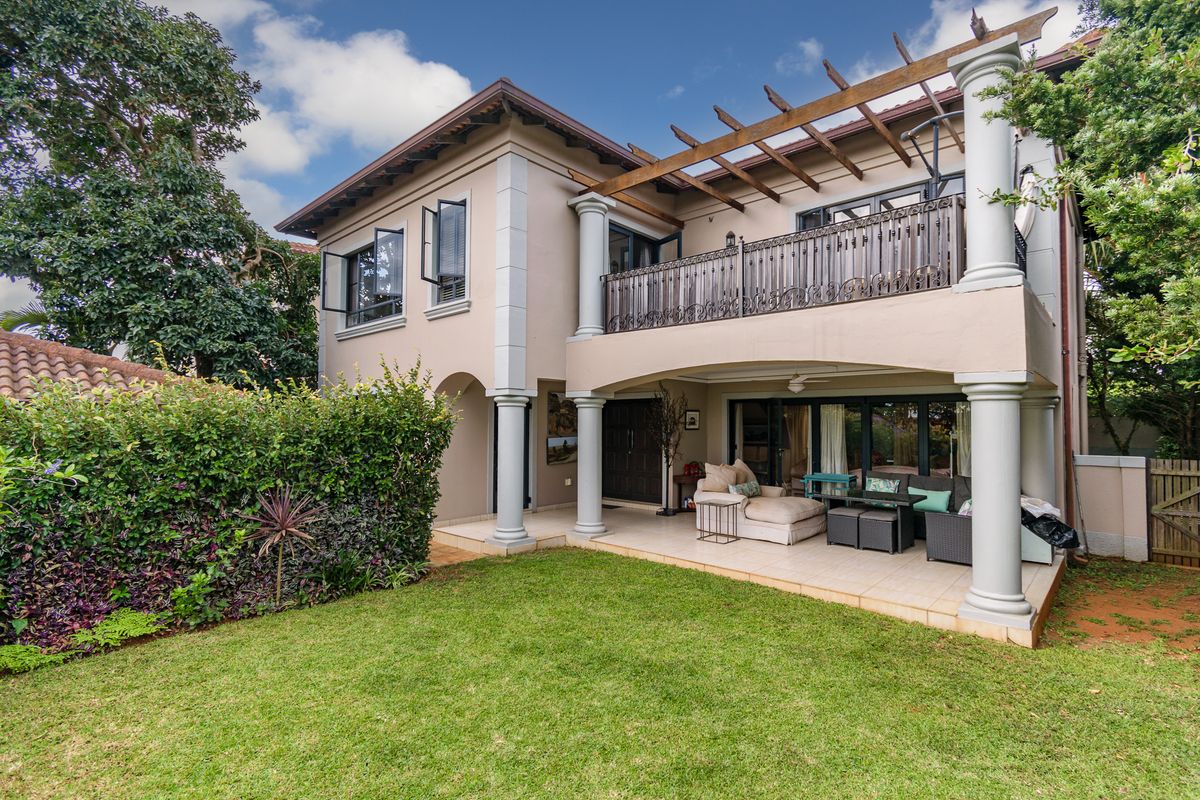 Rear view of a two-story house featuring a covered patio, upper-level balcony with pergola, and a well-maintained garden area.