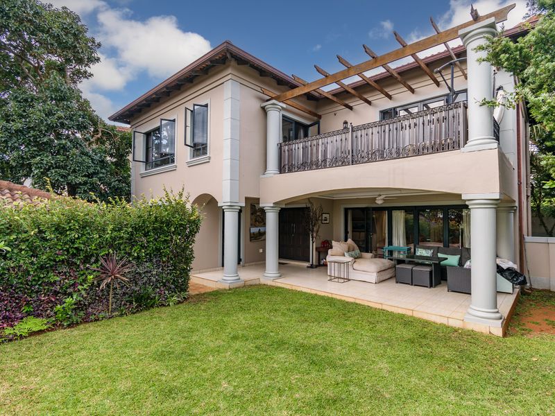 Rear view of a two-story house featuring a covered patio, upper-level balcony with pergola, and a well-maintained garden area.