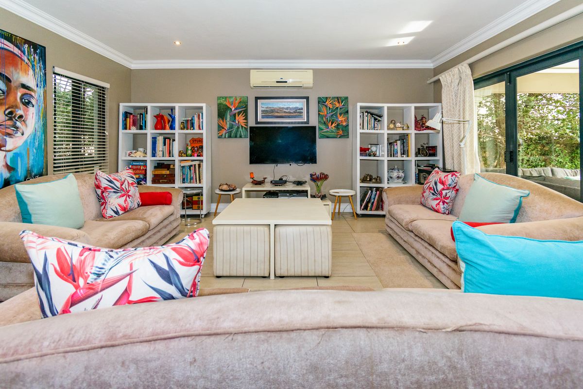 A comfortable living room featuring tiled flooring, crown molding, a wall-mounted air conditioning unit, and large sliding glass doors leading to the patio.