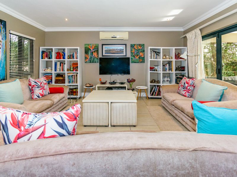 A comfortable living room featuring tiled flooring, crown molding, a wall-mounted air conditioning unit, and large sliding glass doors leading to the patio.