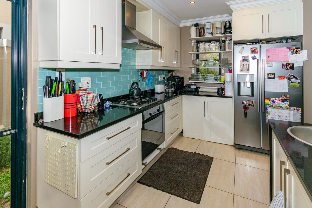 A functional kitchen featuring white cabinetry, black granite countertops, a teal subway tile backsplash, and built-in stainless steel oven and extractor fan.