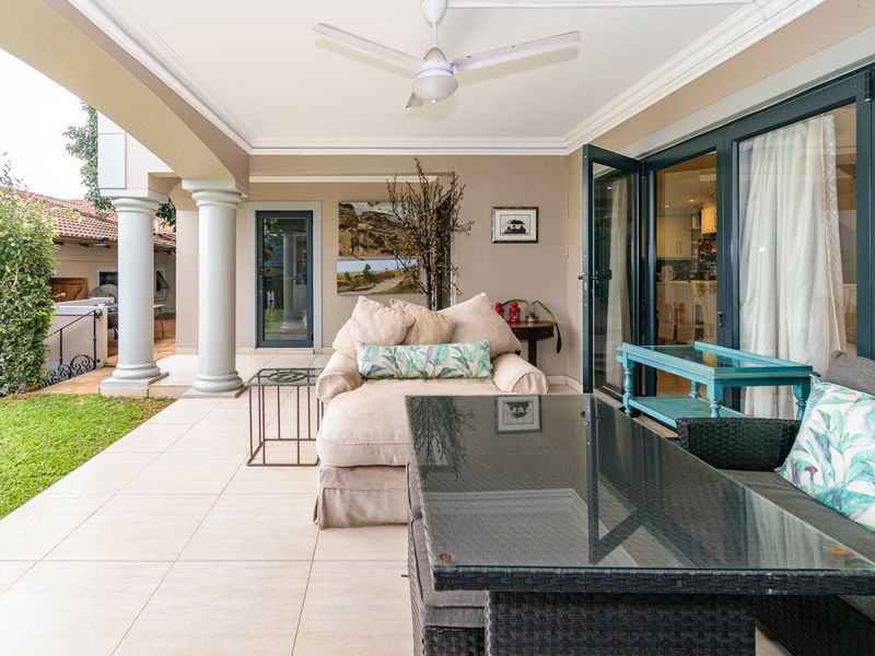 A spacious covered patio featuring tiled flooring, structural columns, and large glass sliding doors providing seamless indoor-outdoor flow.
