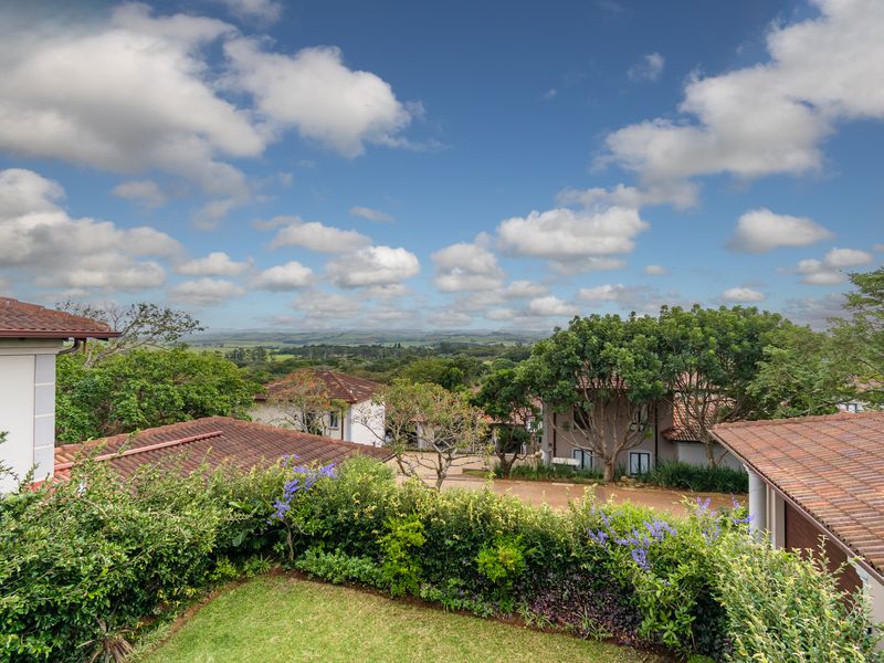 Elevated view overlooking the surrounding estate, featuring lush greenery, tiled rooflines, and a scenic landscape under a bright blue sky.