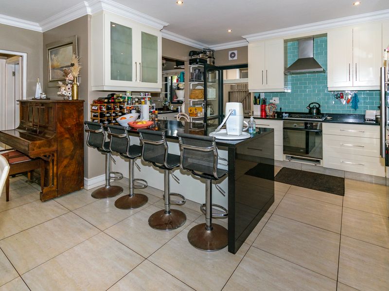 Open-plan kitchen featuring a central island with breakfast bar, stone countertops, tiled backsplash, and built-in oven with extractor fan.
