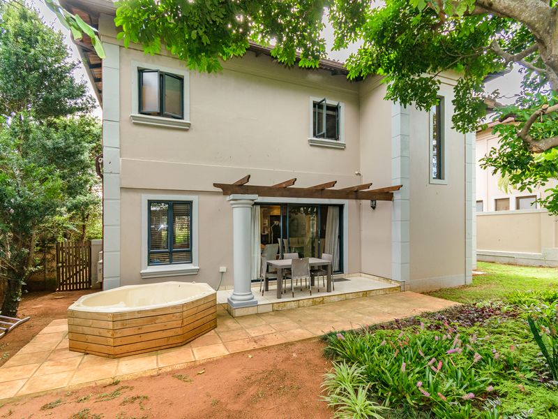 Rear view of the house featuring a paved patio area with a timber pergola, a built-in spa, and a landscaped garden.