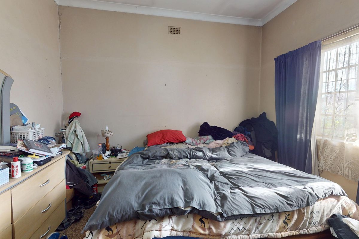 A bedroom featuring a window with security bars and a ventilation grille, requiring cosmetic updates to the wall finishes.